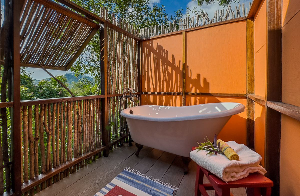 Outdoor clawfoot bathtub on a bamboo-enclosed terrace with orange walls and lush jungle views.
