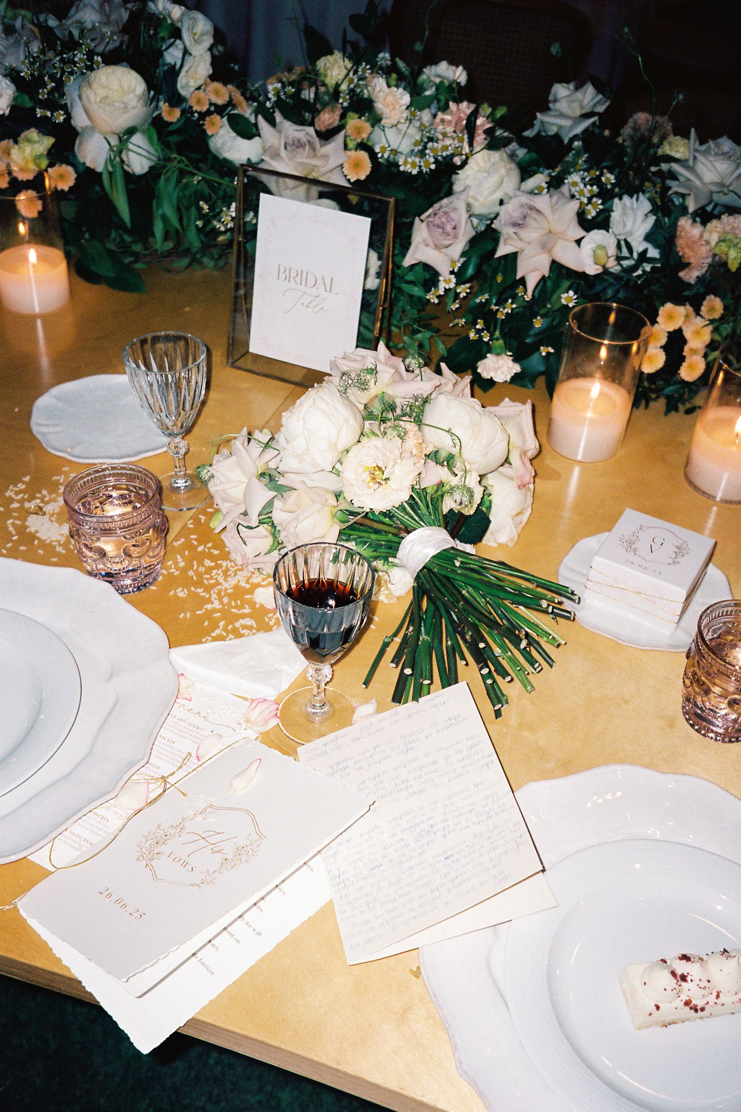 Elegant wedding reception table with white floral centerpiece, candles, gold runner, and handwritten menus.