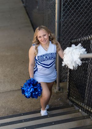 Rockville cheerleader smiling with blue and white pom-poms on stadium steps.