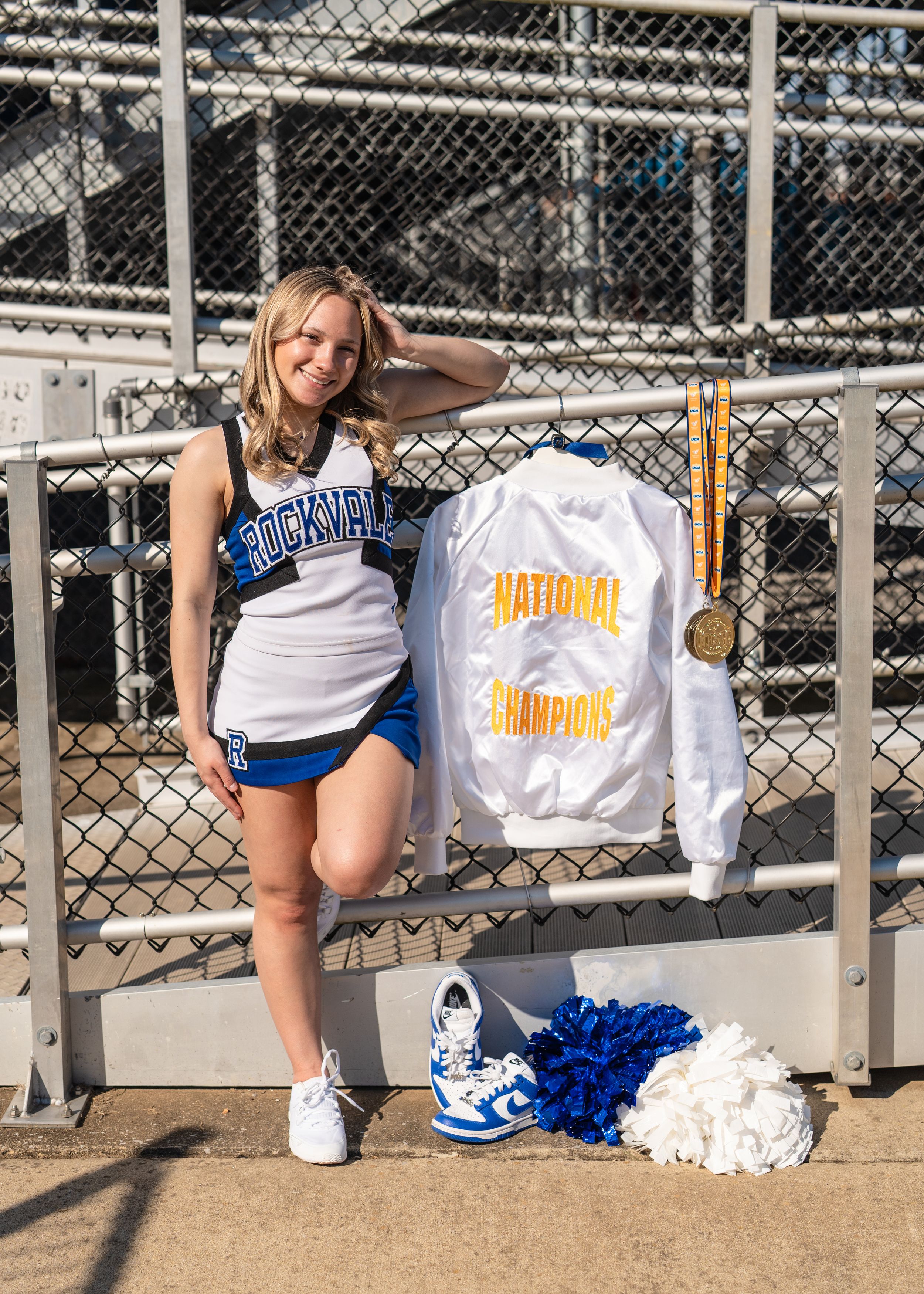 Rockville cheerleader posing with National Champions jacket, medal, and pom-poms.