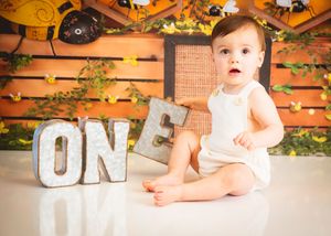 Baby's first birthday photo with marquee ONE letters on white floor with colorful autumn backdrop.