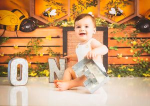 Baby smiling at first birthday cake smash photoshoot holding ONE letters with bee themed orange backdrop.