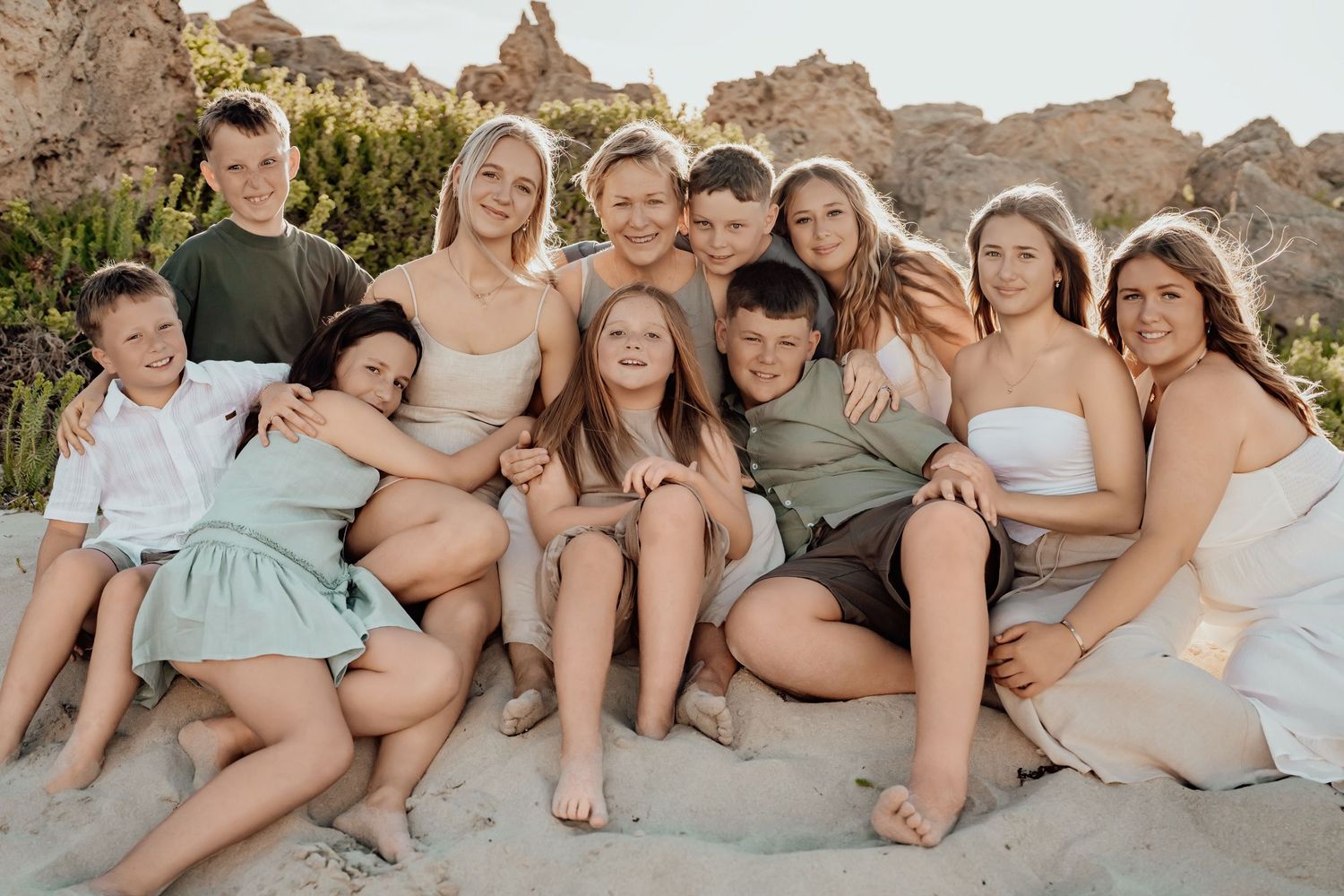 Group sitting together on rocky desert terrain wearing coordinated neutral and pastel colored outfits at sunset.