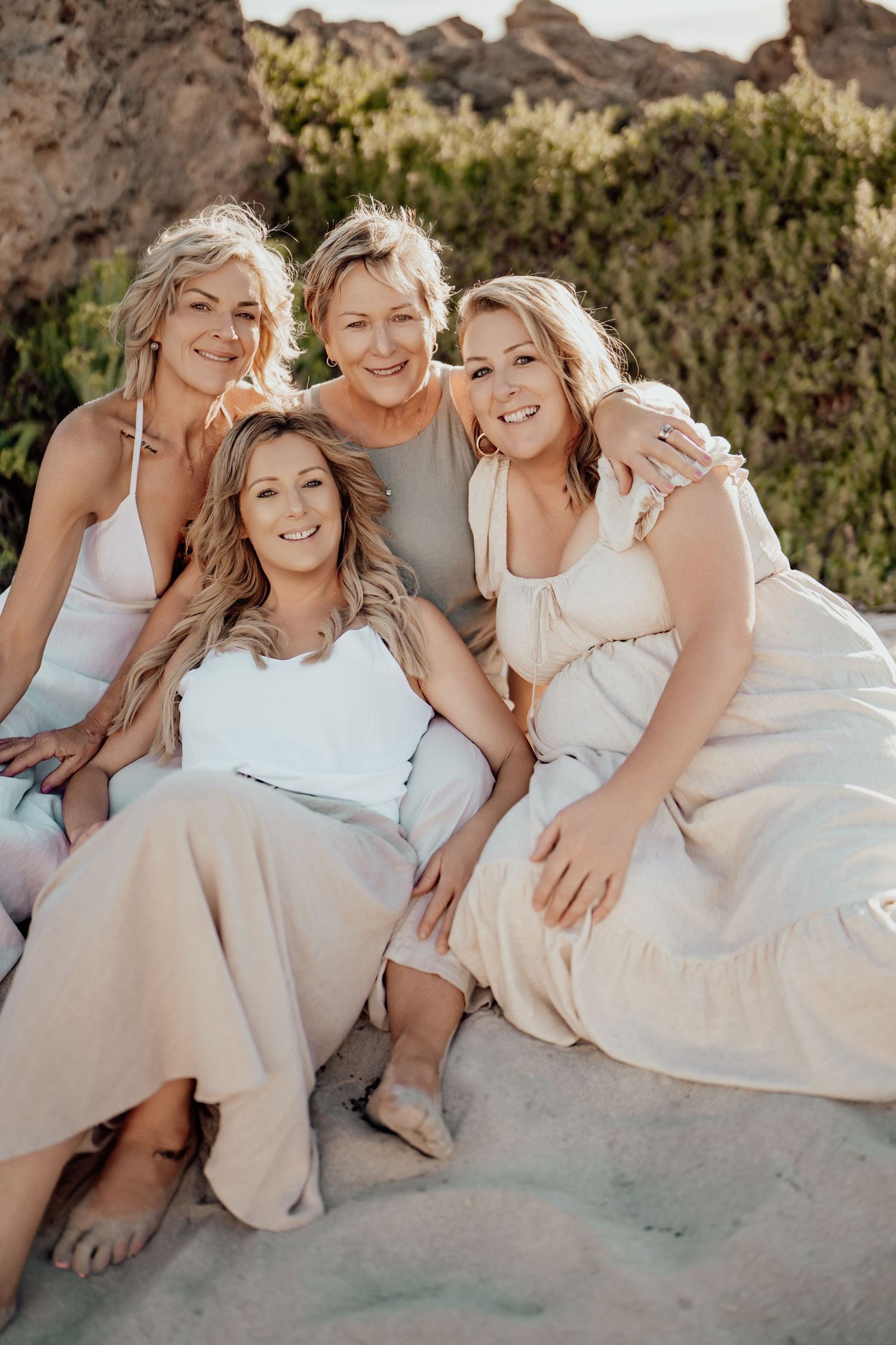 A group wearing white dresses and light colored clothing pose together on a beach during a casual photo session.