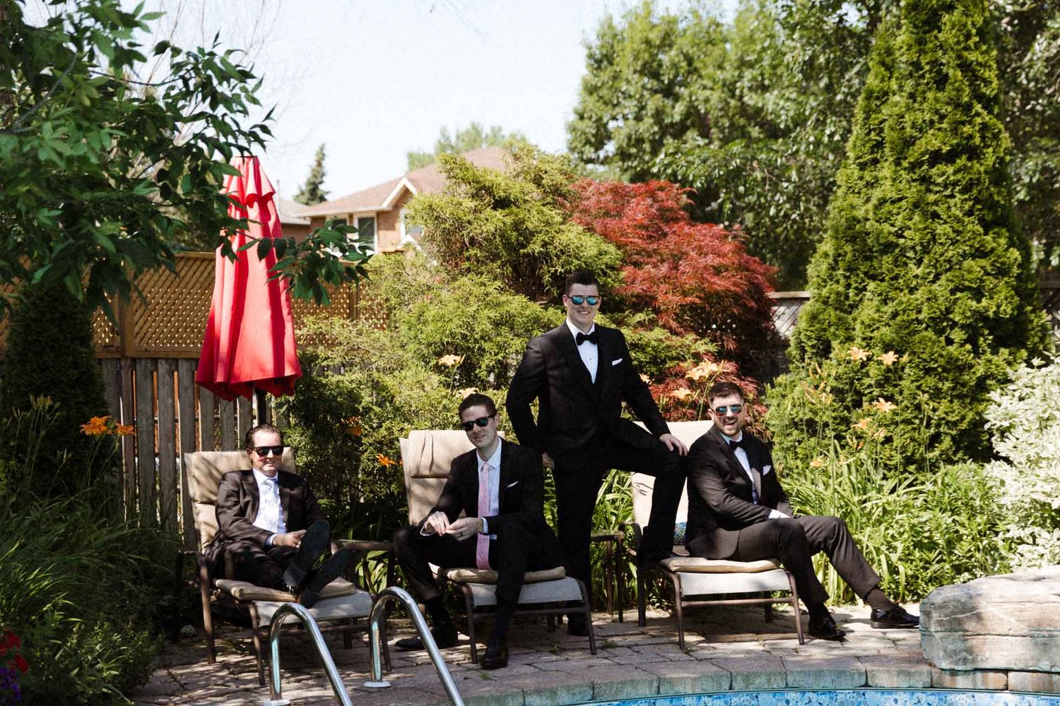 A group gathers in a lush garden setting for an outdoor wedding ceremony on a sunny day.