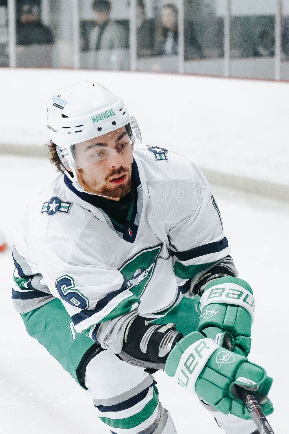 Hockey player in white and teal uniform focused during game play.