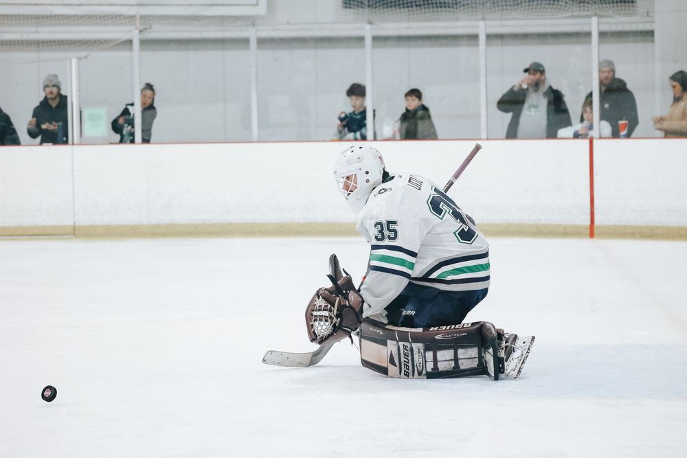 Hockey goalie in number 35 jersey stretches to make save during game.