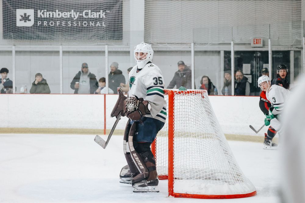 Hockey players compete on an indoor rink with spectators watching through glass barriers.