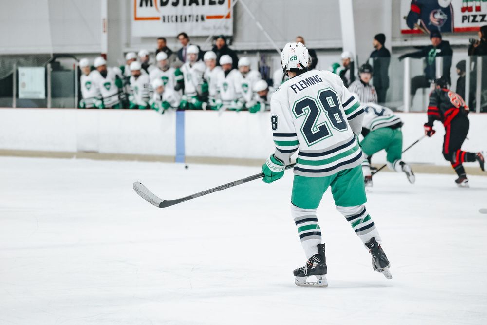 Hockey player in striped green and white uniform positions for play on ice.