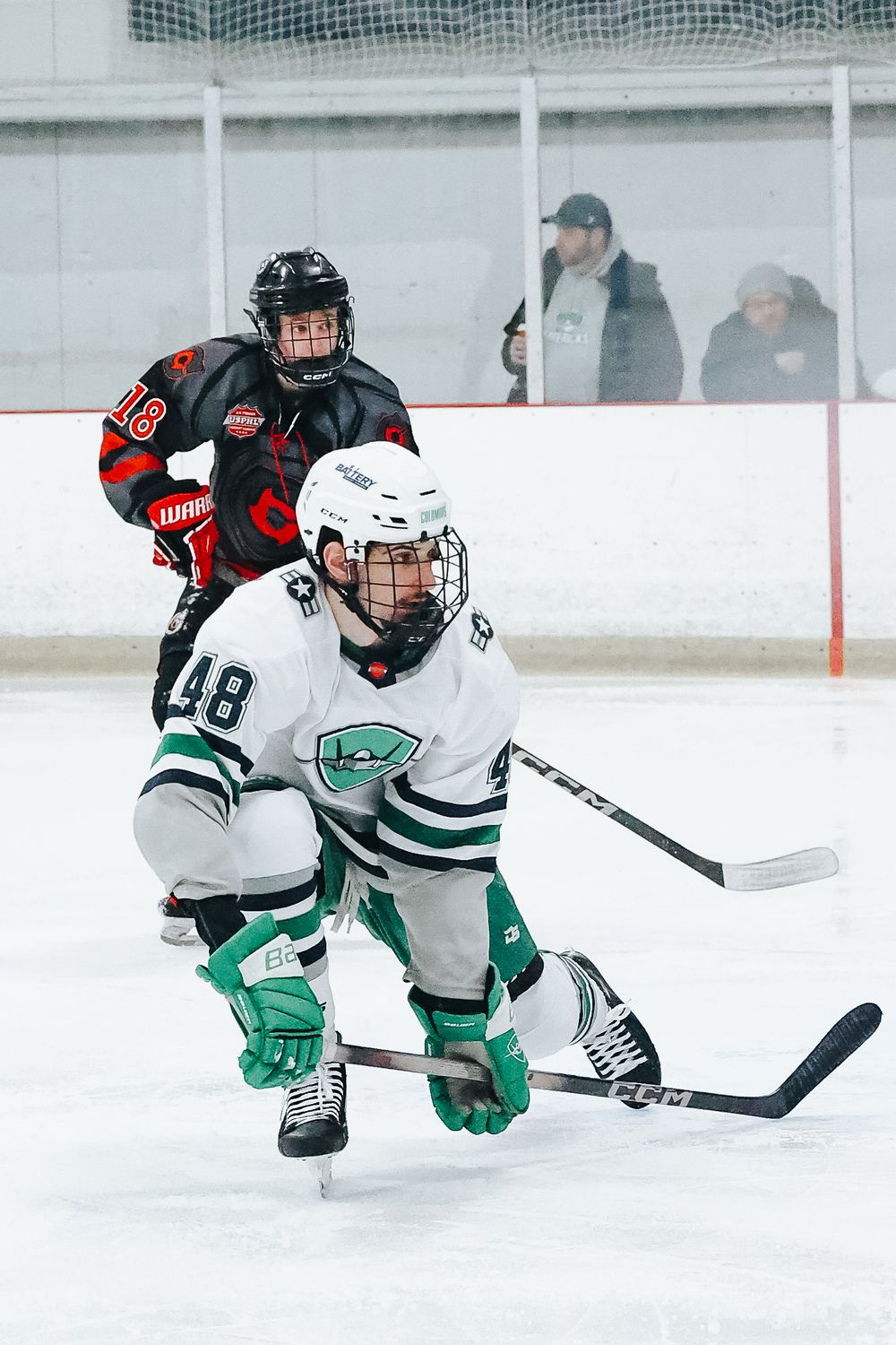 Hockey players in white and green uniforms dive for the puck on the ice.