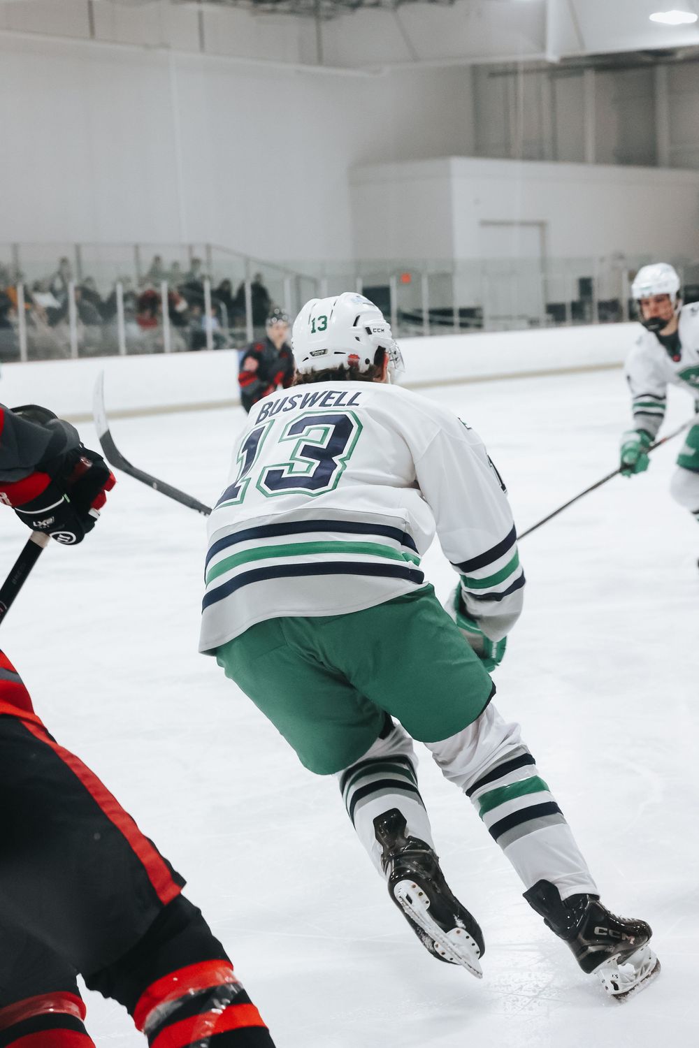 Hockey player in white and green uniform skating at high speed during match.