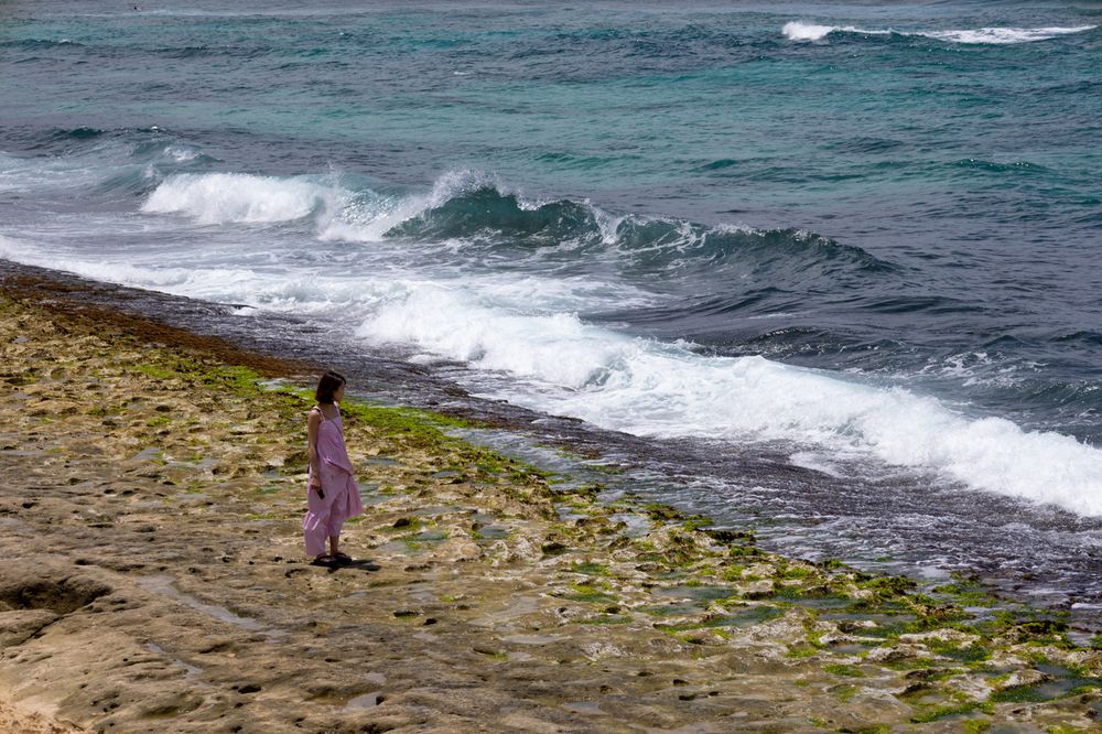 Waves crash along a rocky beach shoreline while people search for seashells on the sandy coast.