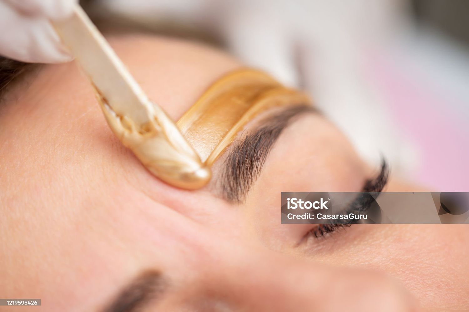 Close up of an eyebrow being groomed with tweezers to remove stray hairs and shape the brow line.