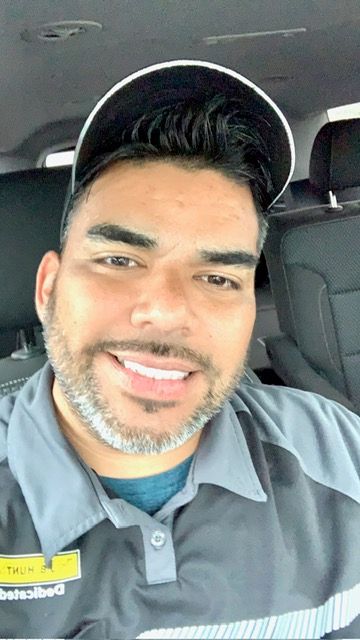 Person in light blue uniform shirt taking car selfies while smiling at the camera.
