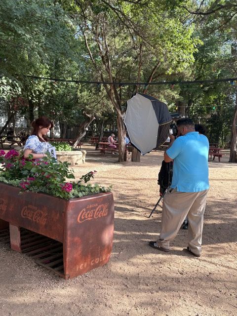 A photographer sets up lighting equipment near a rustic metal planter box in an outdoor garden setting.