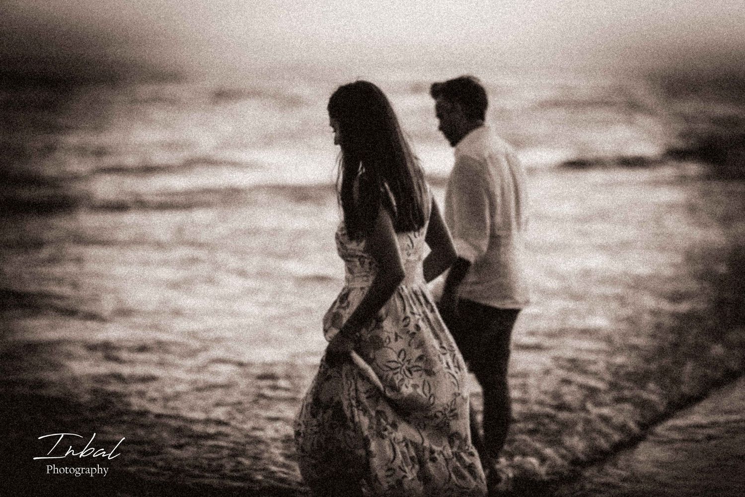 Old grain sepia photo of a couple holding hands walking on the beach.