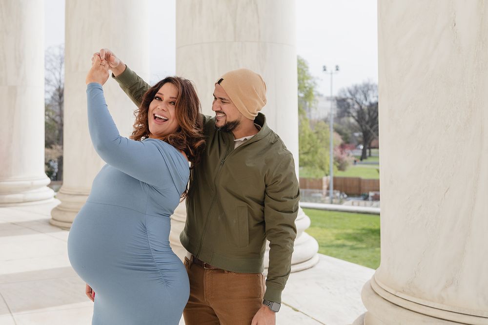 A couple in casual attire shares a joyful moment while walking together outdoors near white columns.