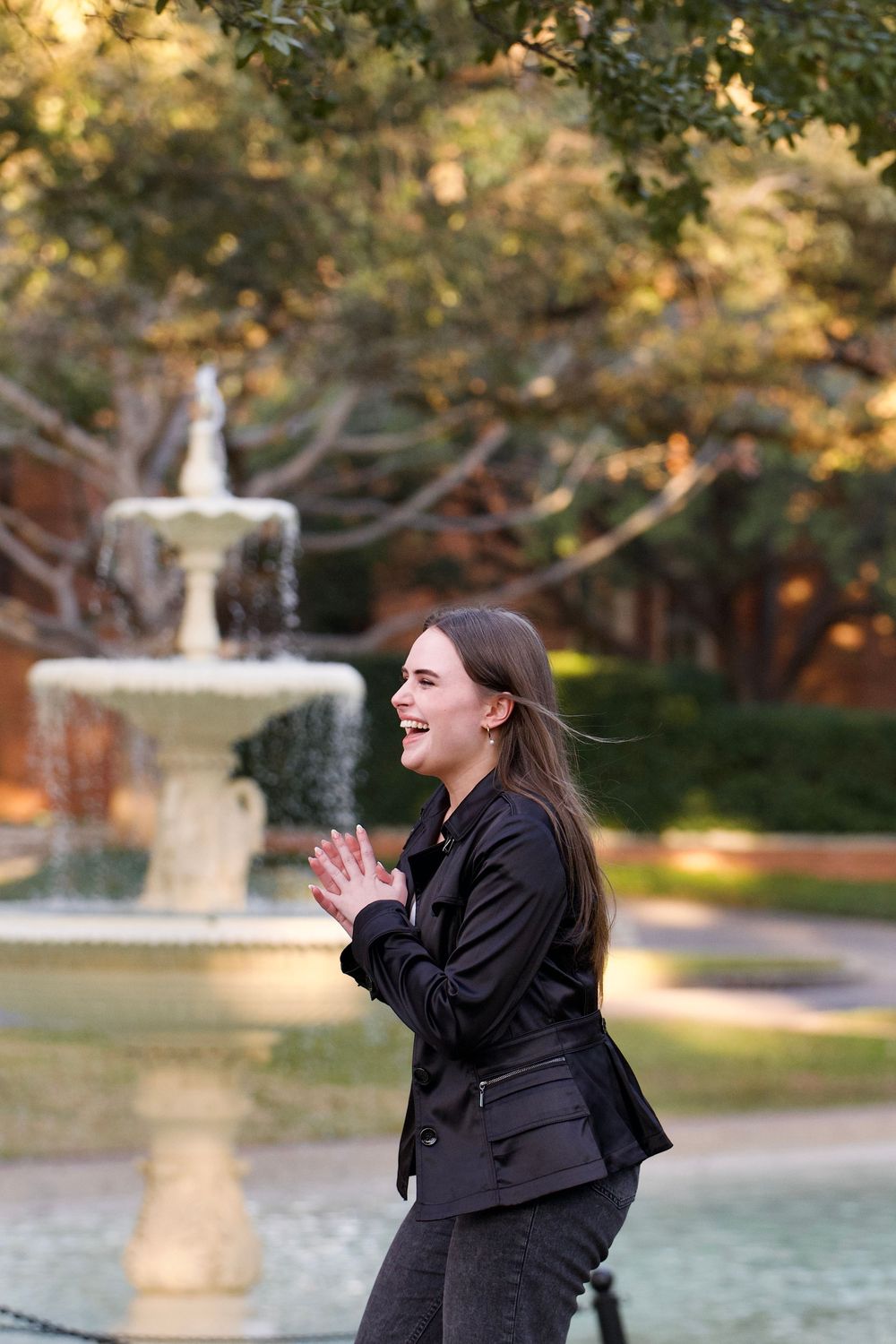 Happy young woman clapping hands near decorative fountain in park.