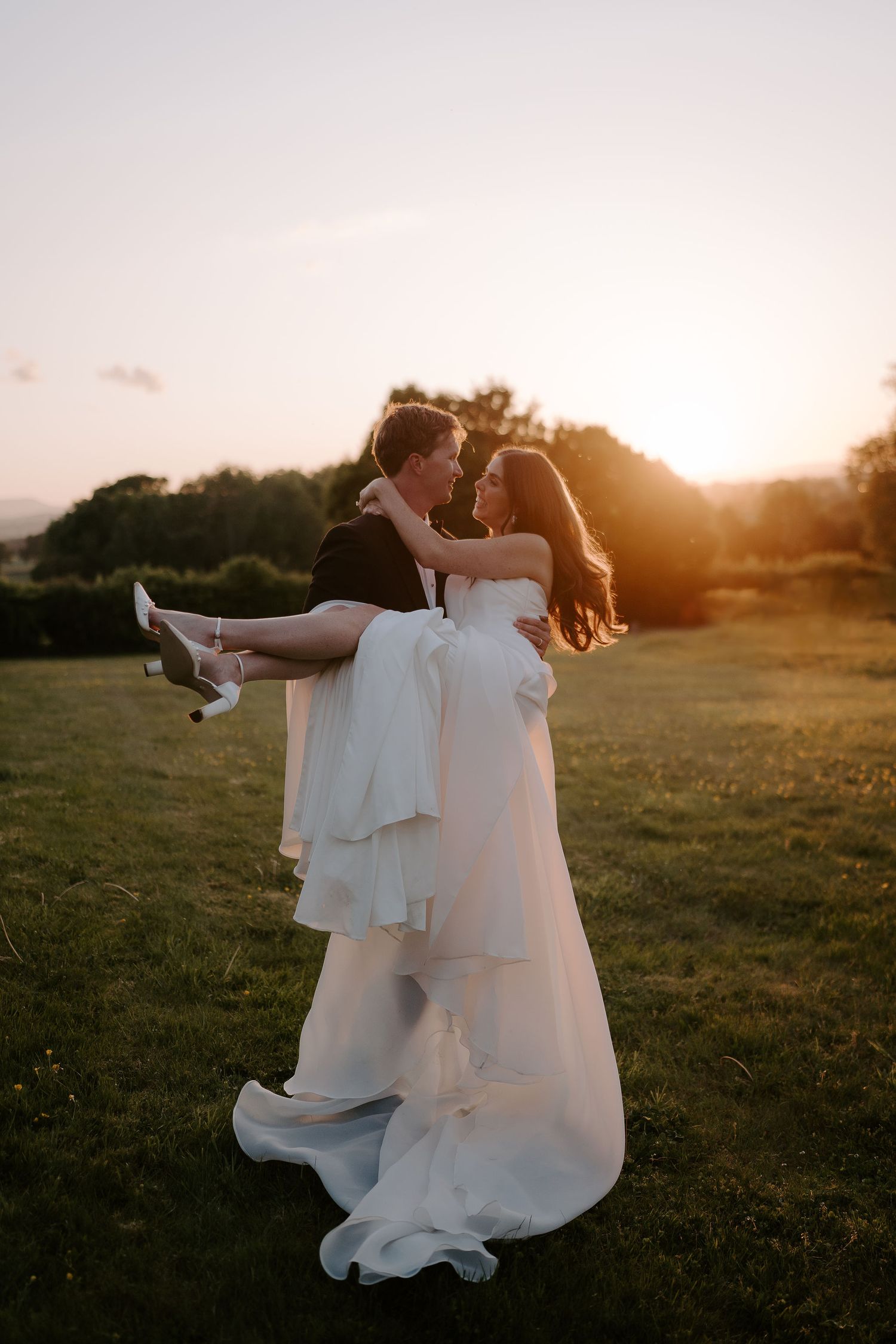 groom carrying bride across the lawn in the setting sun at dewsall court in herefordshire