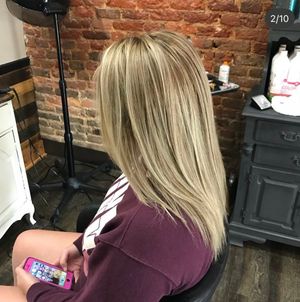 Straight blonde hair styled with dimensional highlights against exposed brick wall in salon setting.