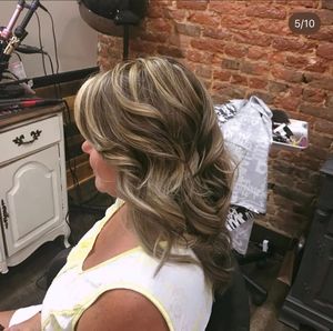 Close-up view of a hairstyling session at a salon with exposed brick wall background.
