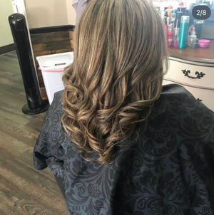 Long wavy brown hair with caramel highlights styled in loose curls cascading down the back.