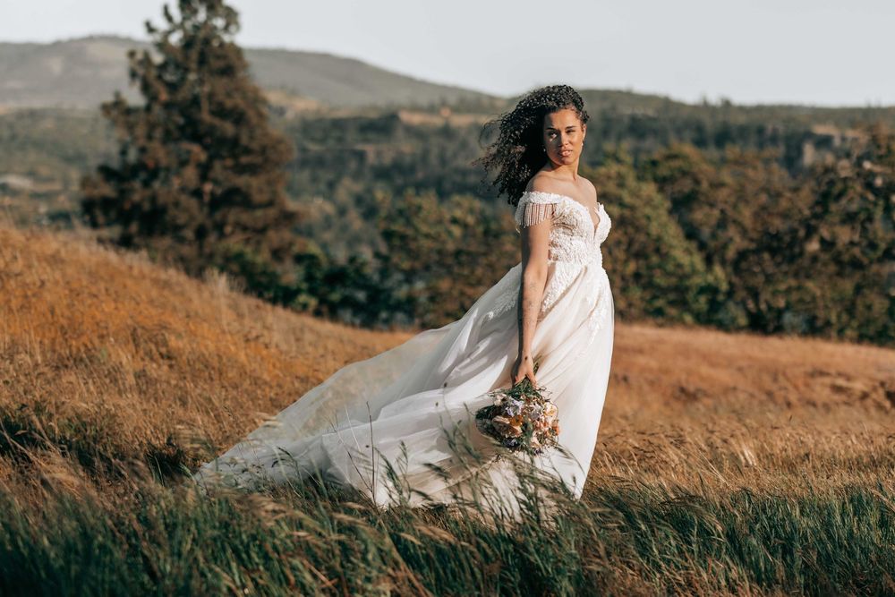 Ellensburg, WA wedding bride standing posing for the camera in a grassy field with wind blowing her hair and dress.
