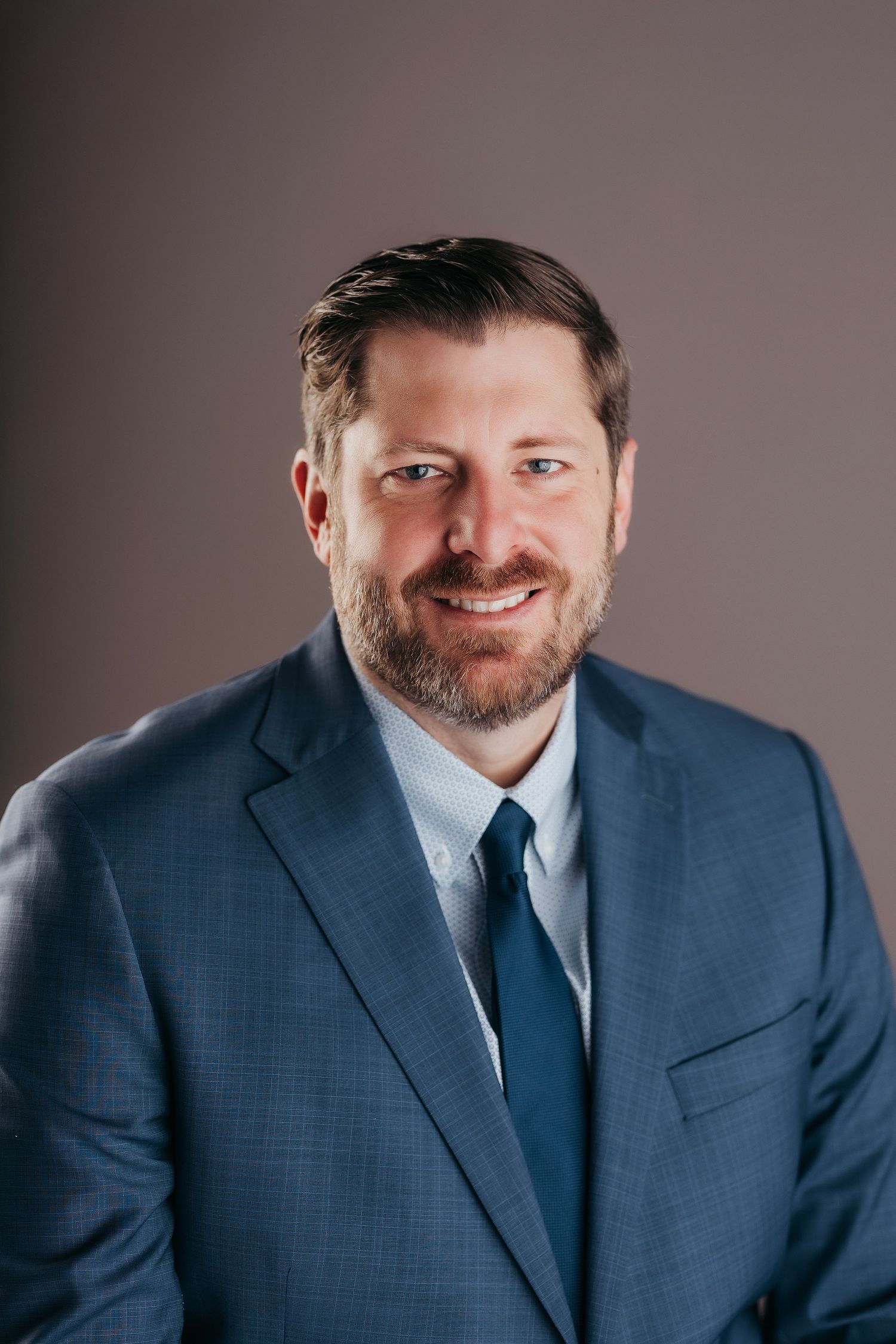 Professional headshot series showing a person in a navy blue suit and tie against a gray studio background.