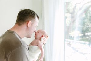 A tender moment between parent and newborn baby by a bright window in natural light.