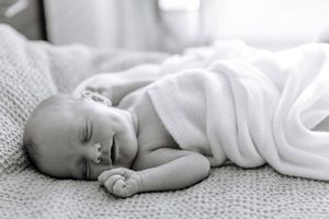 A peaceful sleeping newborn baby wrapped in a soft white blanket rests on textured bedding.
