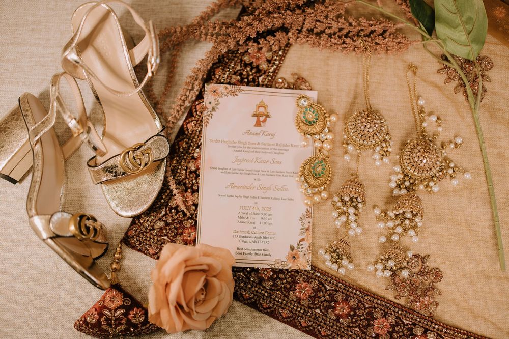 Wedding invitation with gold jewelry, beige sandals, and a peach rose on textured fabric background.