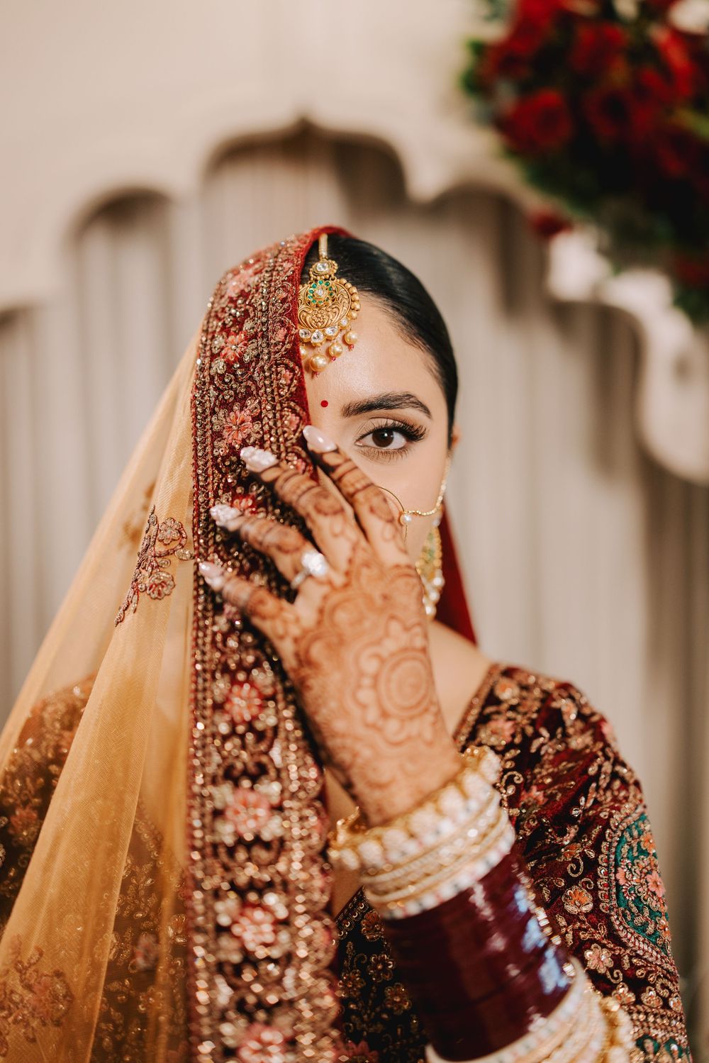 Close-up view of traditional Indian bridal jewelry and henna details in deep burgundy and gold tones.