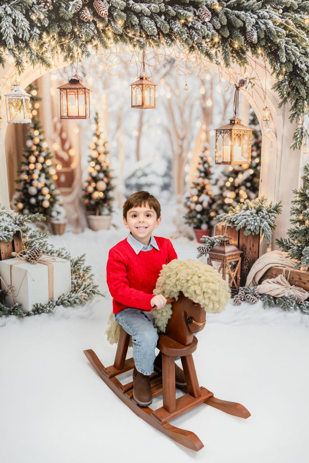 A festive winter scene with a wooden rocking horse, decorated Christmas trees, and hanging lanterns in a snowy setting.