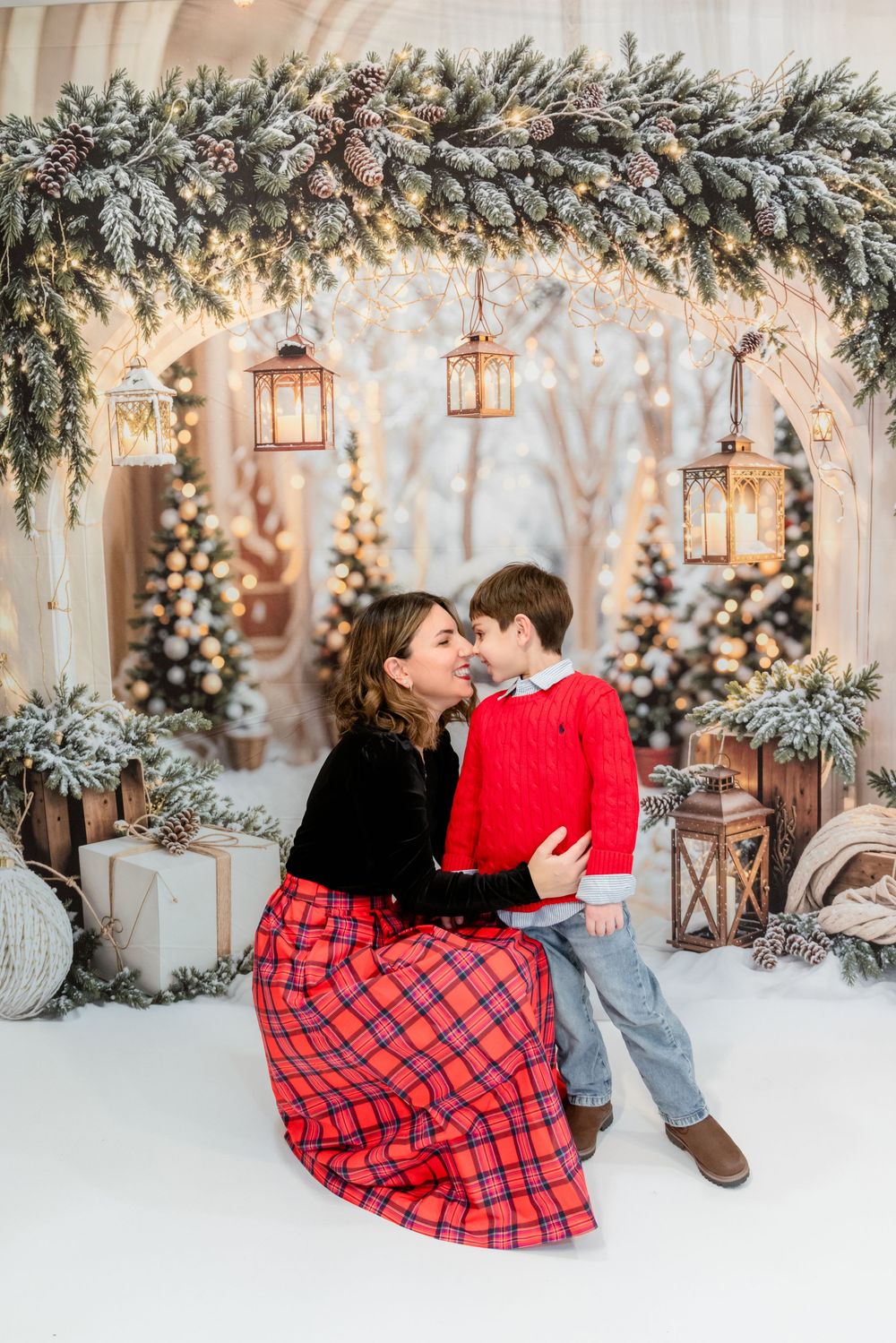 A romantic winter photo session with hanging lanterns, snow-covered branches, and cozy plaid blankets creating a magical atmosphere.