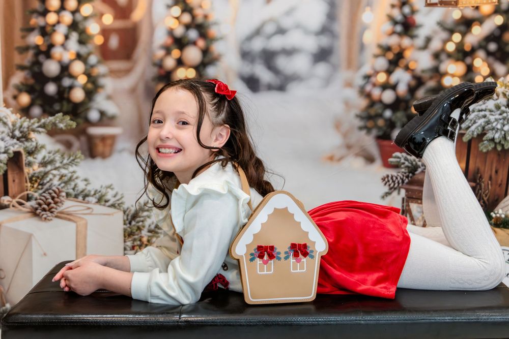A child lies on the floor during a festive holiday photoshoot with Christmas lights and decorations in the background.