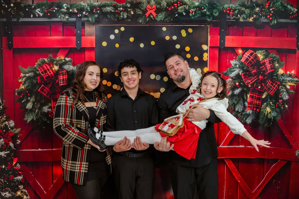 Holiday family portraits in front of red backdrop with festive Christmas decorations and greenery.