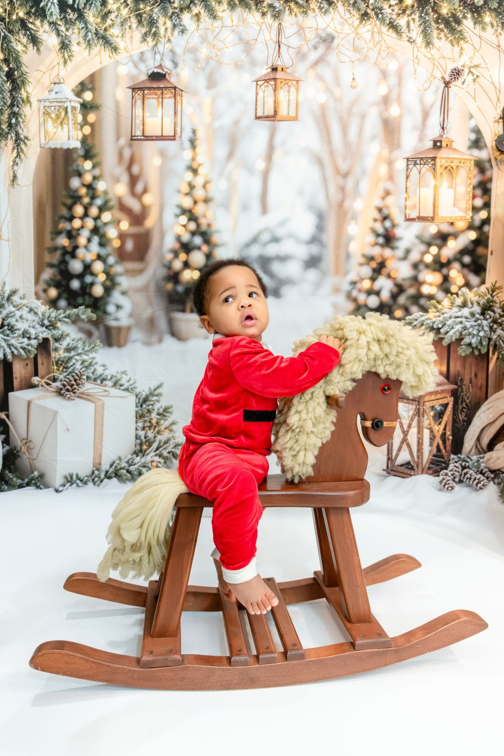 Festive holiday scene with wooden rocking horse, hanging lanterns, and decorated Christmas trees in snowy setting.