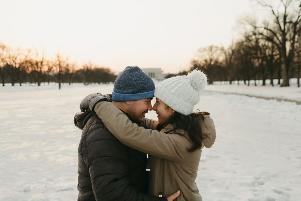 A romantic winter scene with a couple embracing in a snowy landscape at sunset.