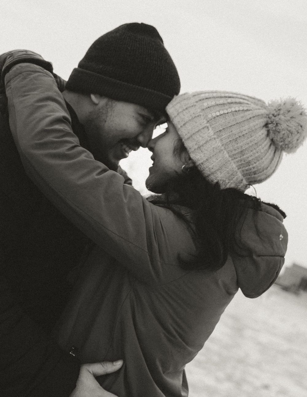 A tender moment between two people wearing winter hats and coats in the snow.