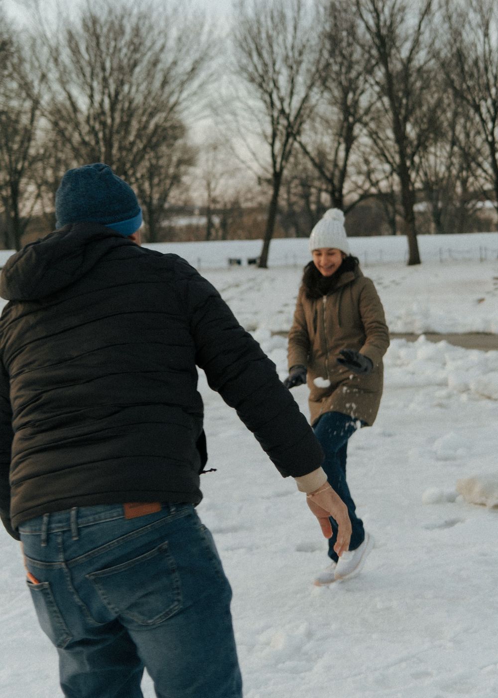 Two people having fun throwing snow at each other in a snowy winter park landscape.