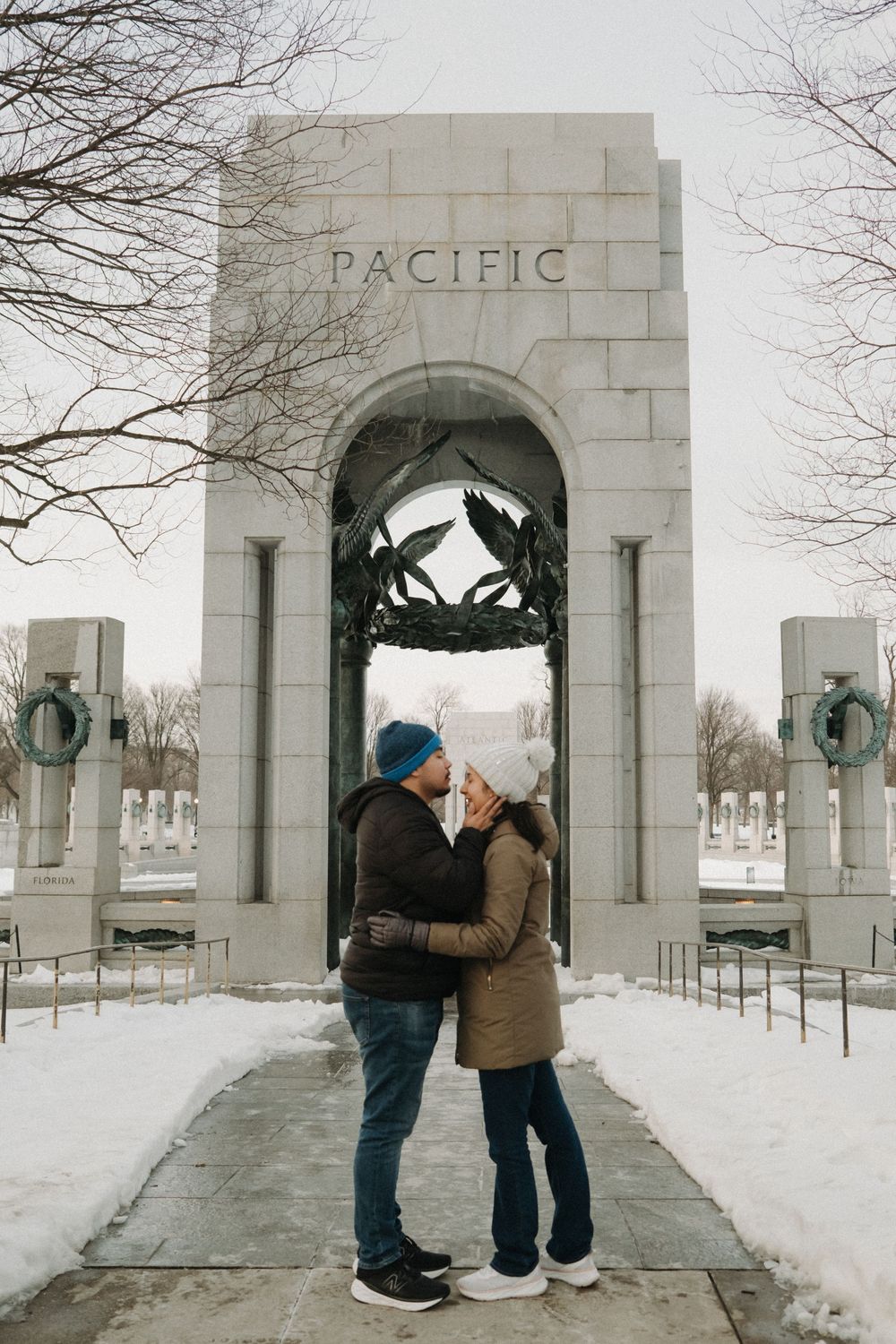 A couple shares an intimate moment under the Pacific memorial arch in winter snow.