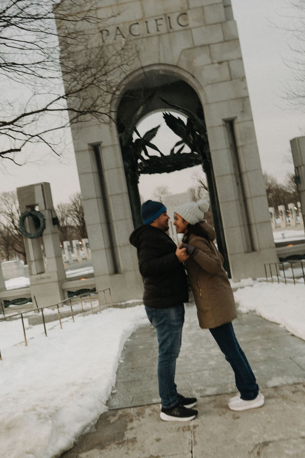 A couple shares a tender moment under a stone archway in the snow.