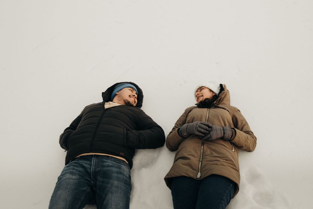 Two people lie in the snow making snow angels during a winter day.