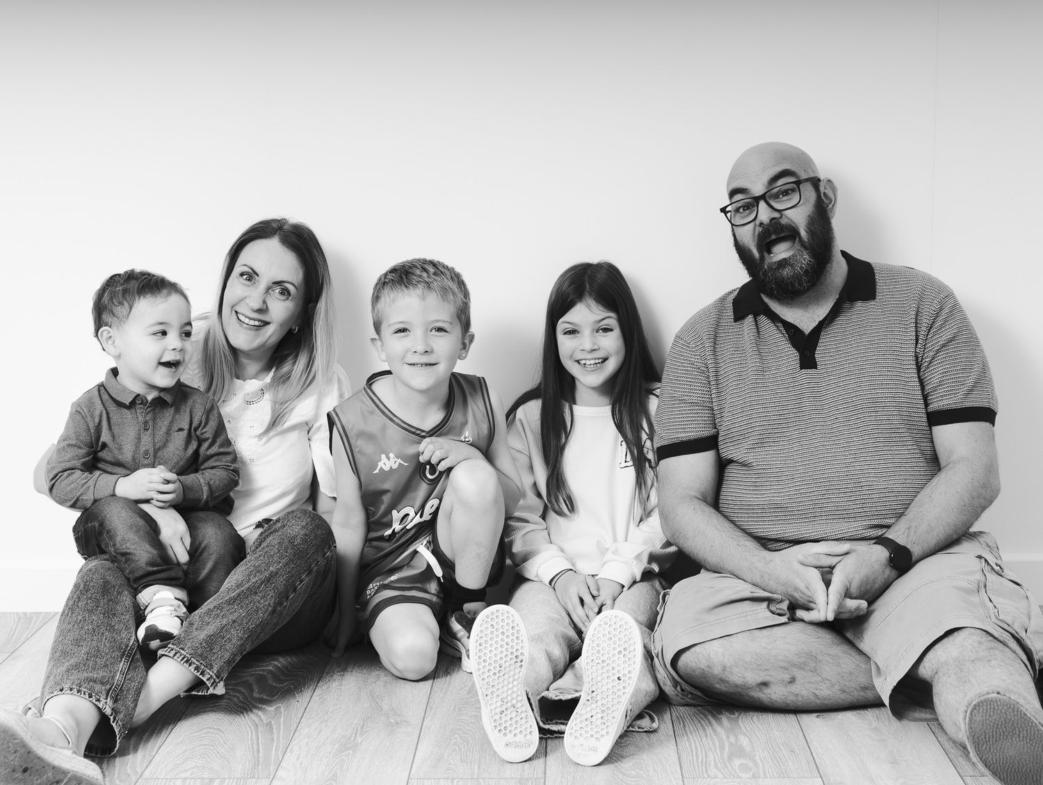 A black and white portrait of a family of five sitting together against a plain wall.