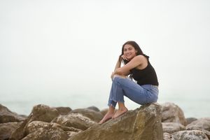 Person in casual wear sitting thoughtfully on coastal rocks by the ocean.