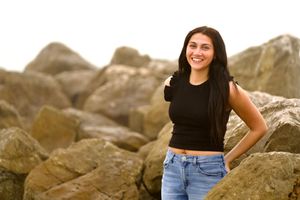 Person in black crop top and jeans posing confidently on rocky beach formation.