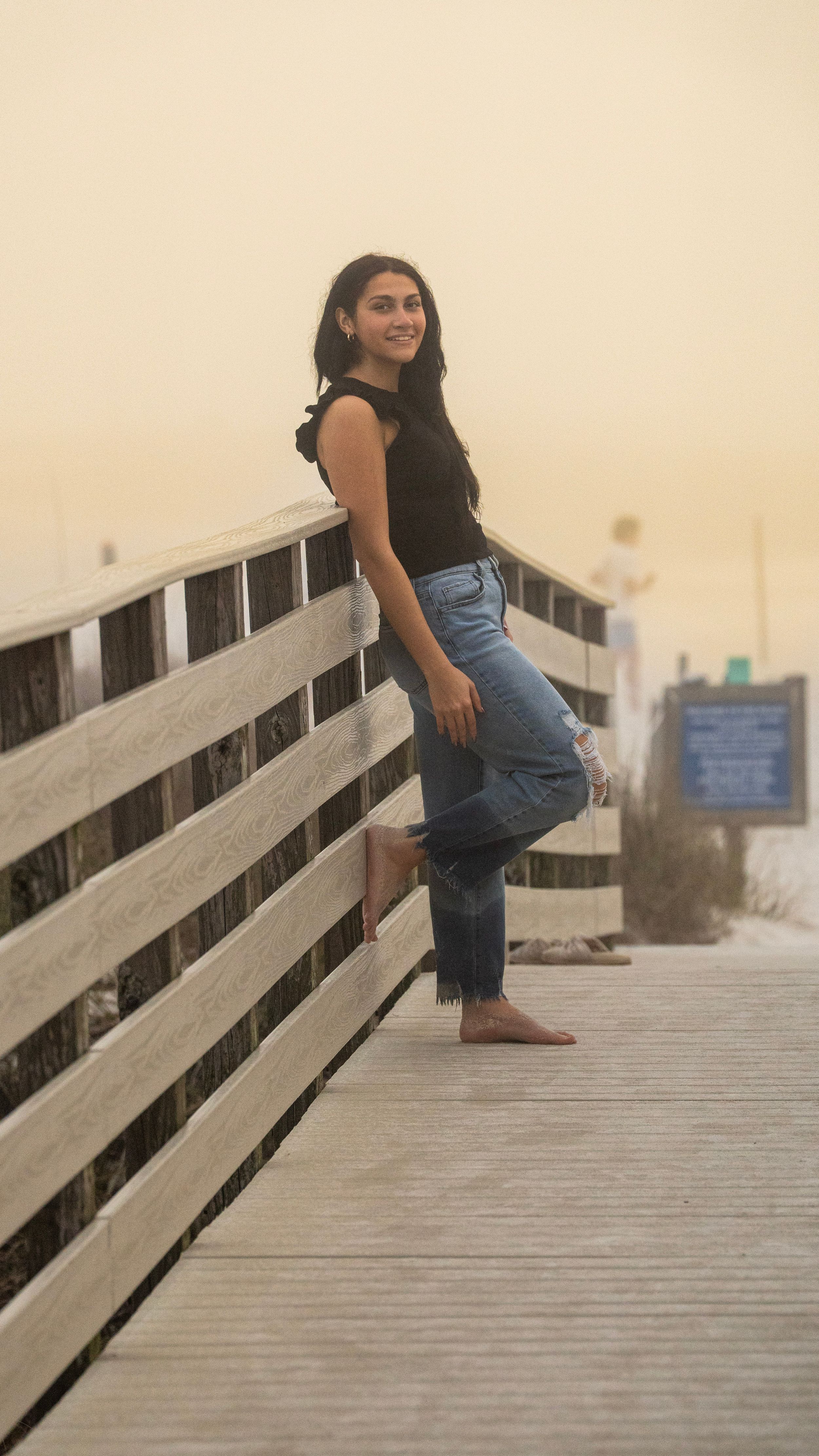 Person in casual attire leaning against wooden boardwalk railing at dusk.