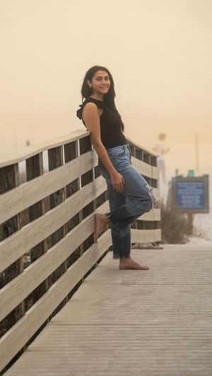 Person in casual attire leaning against wooden boardwalk railing at dusk.