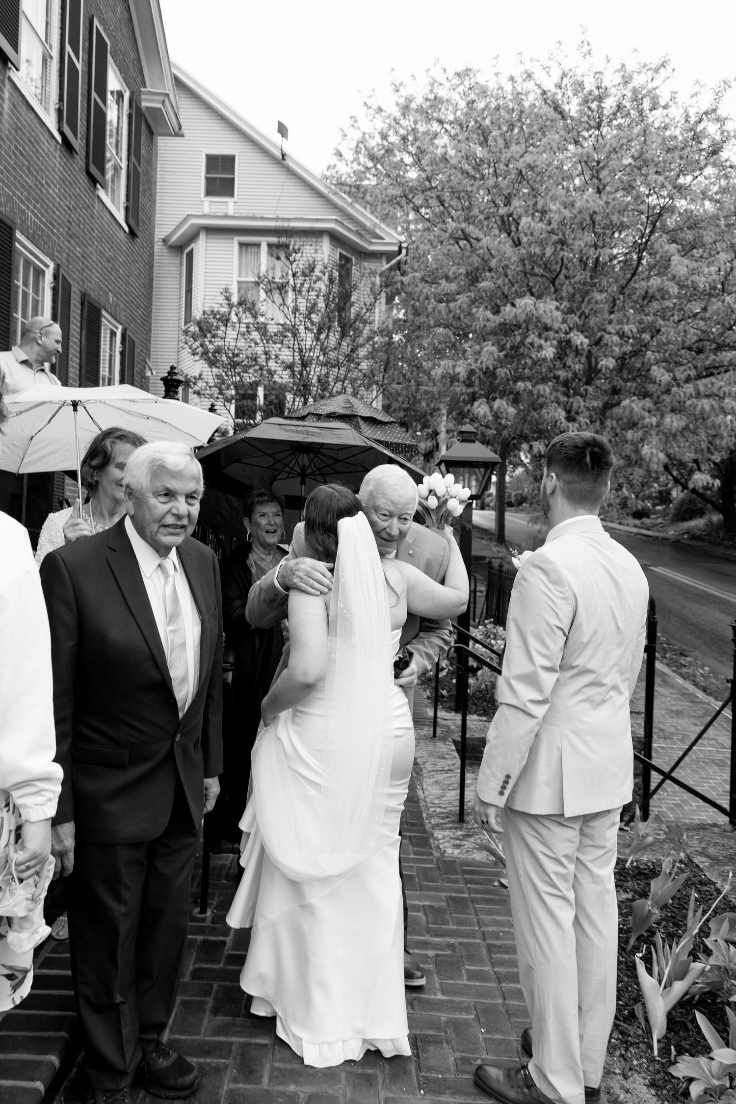 Bride walks to groom in outdoor rainy wedding ceremony with family escort.