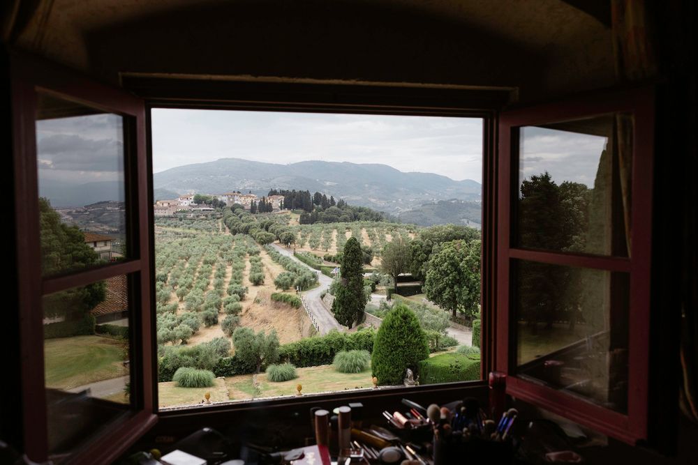 View through rustic window overlooking Tuscan countryside with rolling hills, olive groves and cypress trees in Tenuta di Artimino